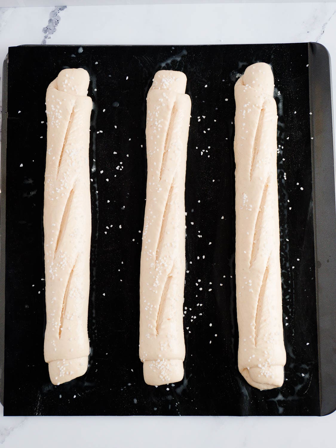 Dinkel-Laugenbaguettes Teiglinge mit Hagelsalz bestreuen