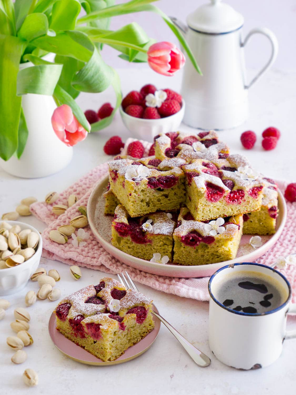 Protein Pistazienkuchen mit Himbeeren in Stückchen geschnitten auf einem Teller, davor liegt ein einzelnes Stückchen auf einem kleinen Tellerchen