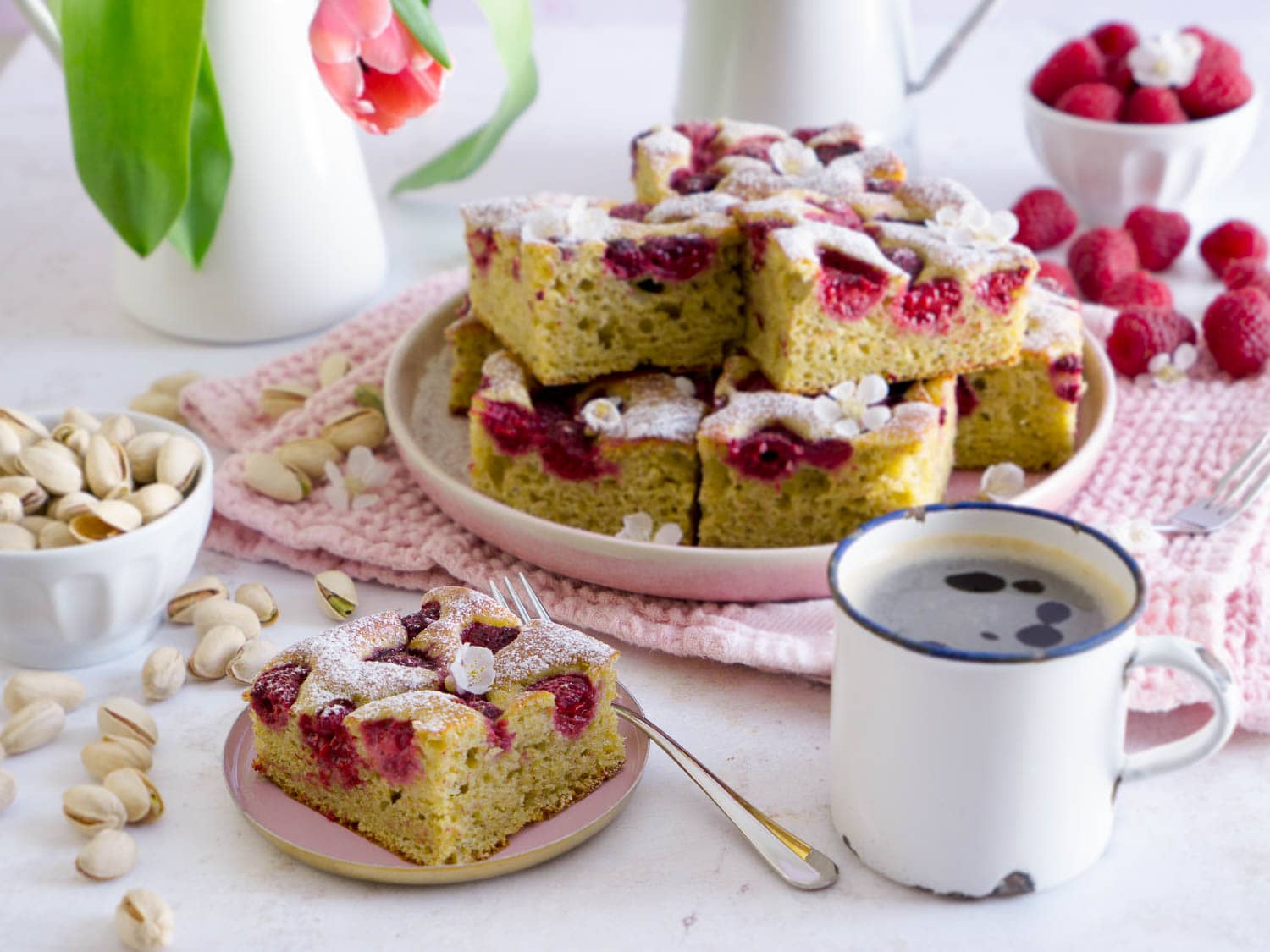 Protein Pistazienkuchen mit Himbeeren in Stückchen geschnitten auf einem Teller, davor liegt ein einzelnes Stückchen auf einem kleinen Tellerchen